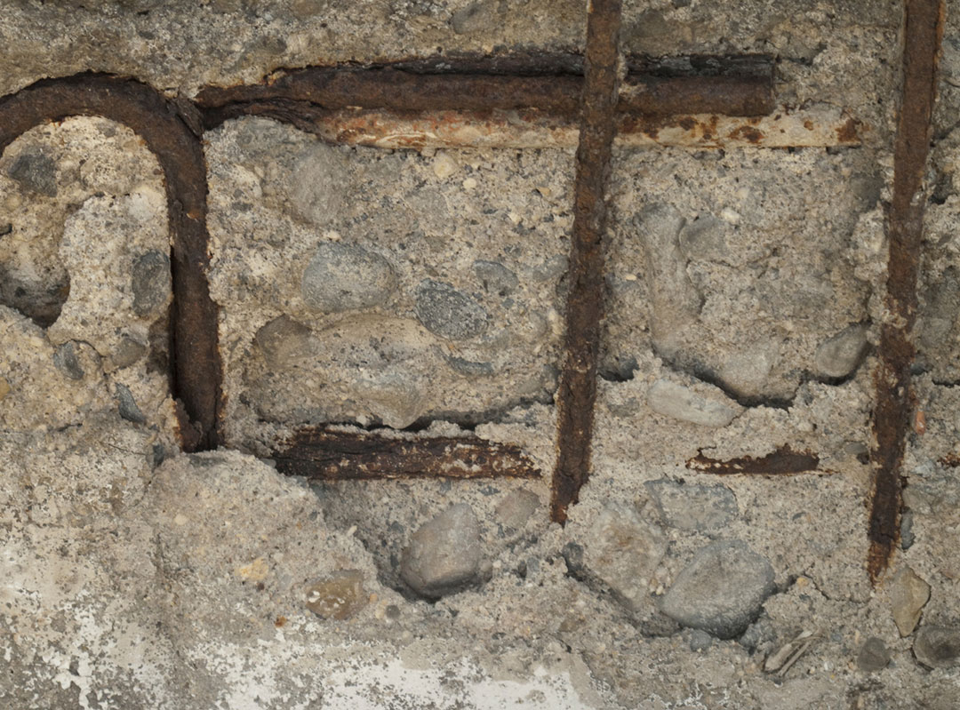 Severely deteriorated concrete wall revealing corroded steel reinforcement